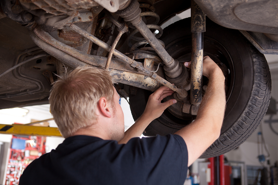 A male mechanic inspecting a CV joint on a car in an auto repair